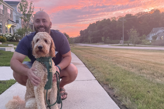 person kneeling by a dog with a colorful pink sky in the background